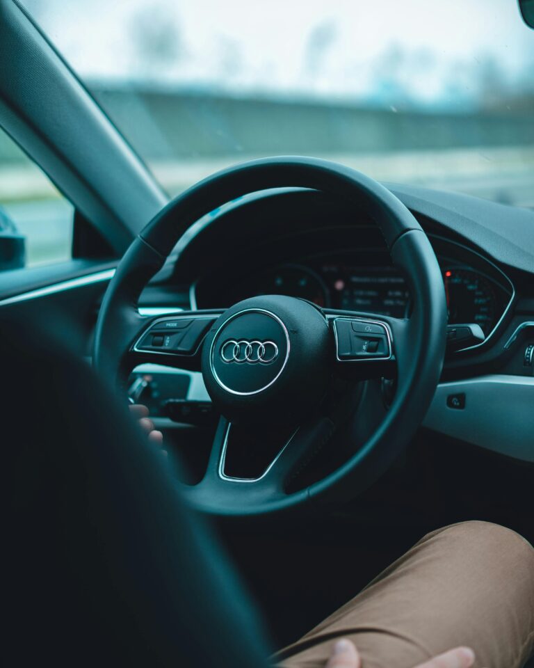 Interior view of an Audi vehicle, focusing on the steering wheel and dashboard while driving. Modern cars like this are often equipped with event data recorders (EDRs), or "black boxes," which store critical driving data to enhance safety, aid in accident investigations, and improve vehicle performance analysis.
