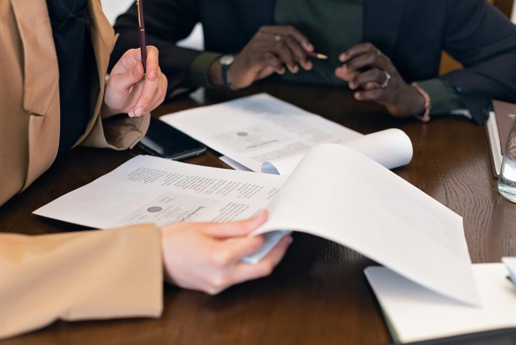 Two professionals reviewing workers' compensation claim documents at a desk, discussing workplace injury risks and legal considerations. Papers with official seals and legal text are visible, emphasizing the importance of compliance and safety measures in reducing recurring claims.