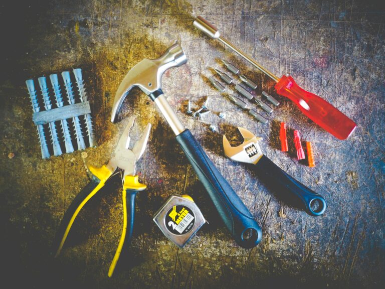 A collection of home repair tools—including a hammer, pliers, adjustable wrench, screwdriver, drill bits, wall plugs, and a measuring tape—spread out on a worn workbench. This image represents the growing cost of home construction materials and labor, emphasizing the need for homeowners to regularly review and update their homeowner’s insurance policy replacement cost limits to avoid being underinsured after a major property loss.