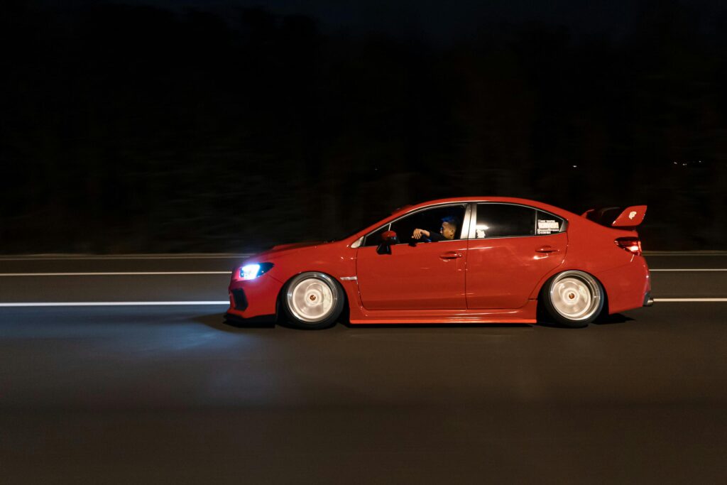 Red sports car driving at night on a highway, highlighting nighttime driving risks and the importance of defensive driving for safety.