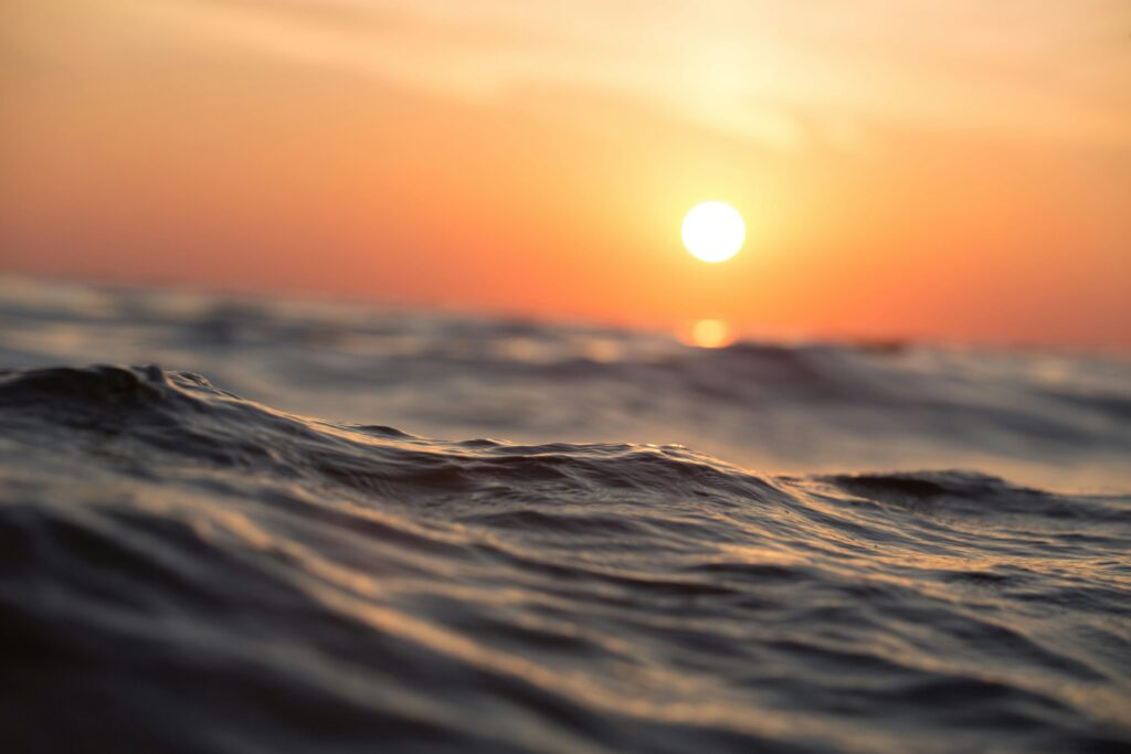 Blazing summer sun setting over ocean waves, symbolizing extreme heat and the importance of recognizing and preventing heat-related illness during hot weather.