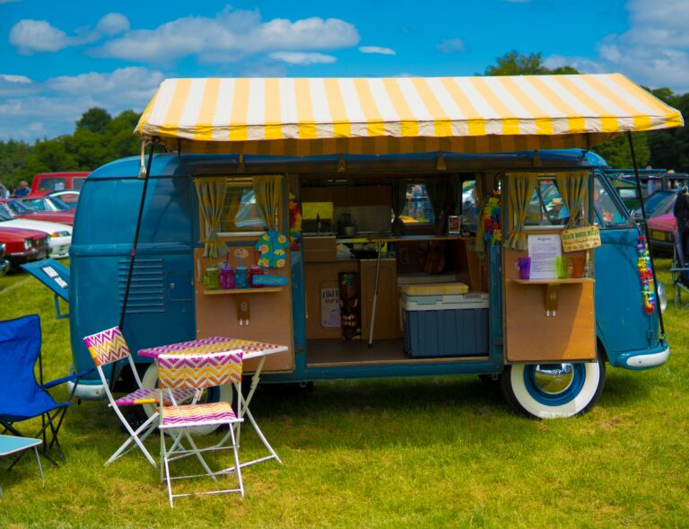 Colorful vintage camper van with awning set up for summer camping, highlighting the importance of insuring fifth-wheels, travel trailers, and pop-up campers.