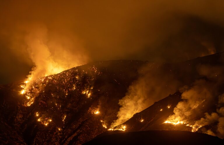 Raging wildfire engulfing a California hillside at night, with thick smoke and flames illustrating the growing wildfire threat impacting homeowner's insurance in Los Angeles.